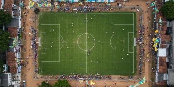Campo de futebol de várzea vibrante com torcida em festa no Brasil em 2025.