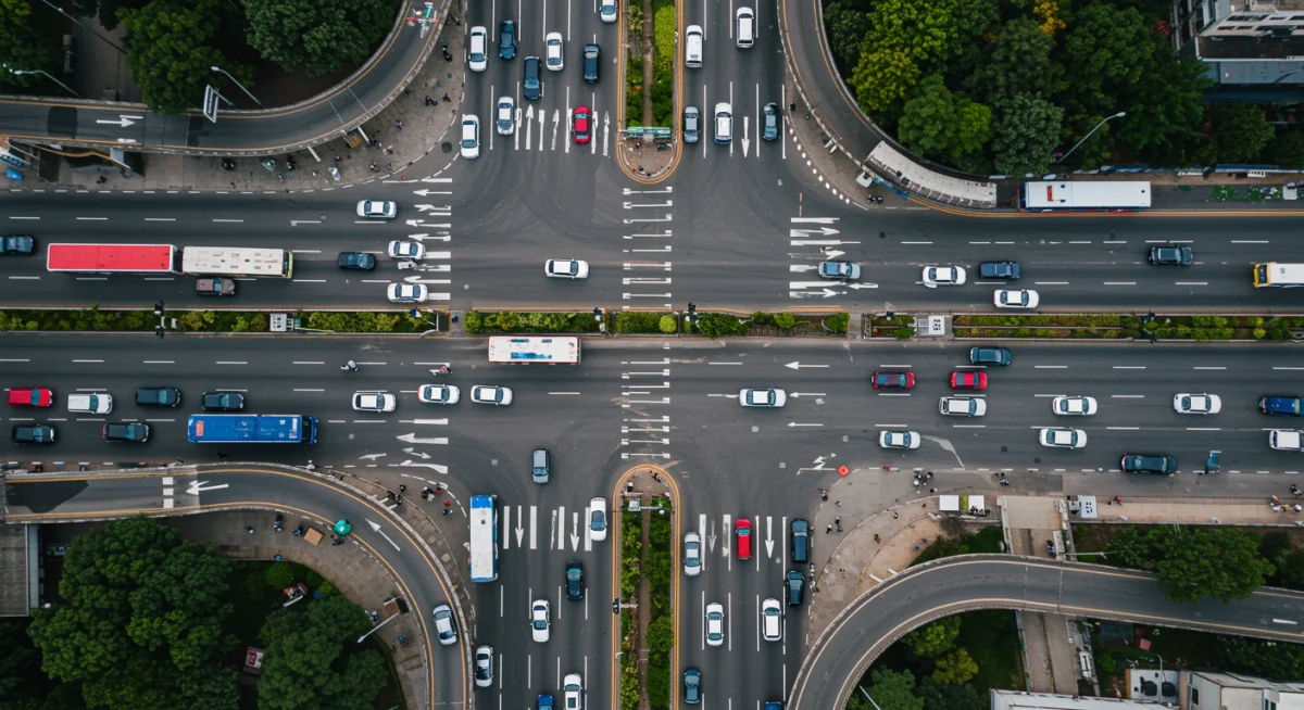 Vista aérea de um cruzamento urbano movimentado com ônibus e carros, representando a complexidade da mobilidade nas grandes cidades.