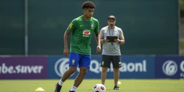 Jovem jogador de futebol brasileiro em campo, observando o futuro com o apoio de um agente.