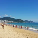 Praia ensolarada no Brasil com pessoas aproveitando o calor do verão de 2025 e o mar calmo.