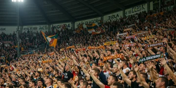 Torcedores vibrantes cantando em um estádio lotado, bandeiras e fumaça colorida ao fundo. A cena reflete a paixão e a energia das torcidas organizadas no futebol brasileiro.