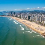 Vista aérea de uma cidade praiana brasileira vibrante, com turistas desfrutando do sol e mar, simbolizando crescimento econômico e atratividade internacional.