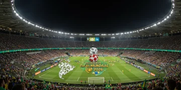 Estádio lotado e iluminado, com o placar exibindo 'Copa do Mundo 2026' e bandeiras sul-americanas vibrando.